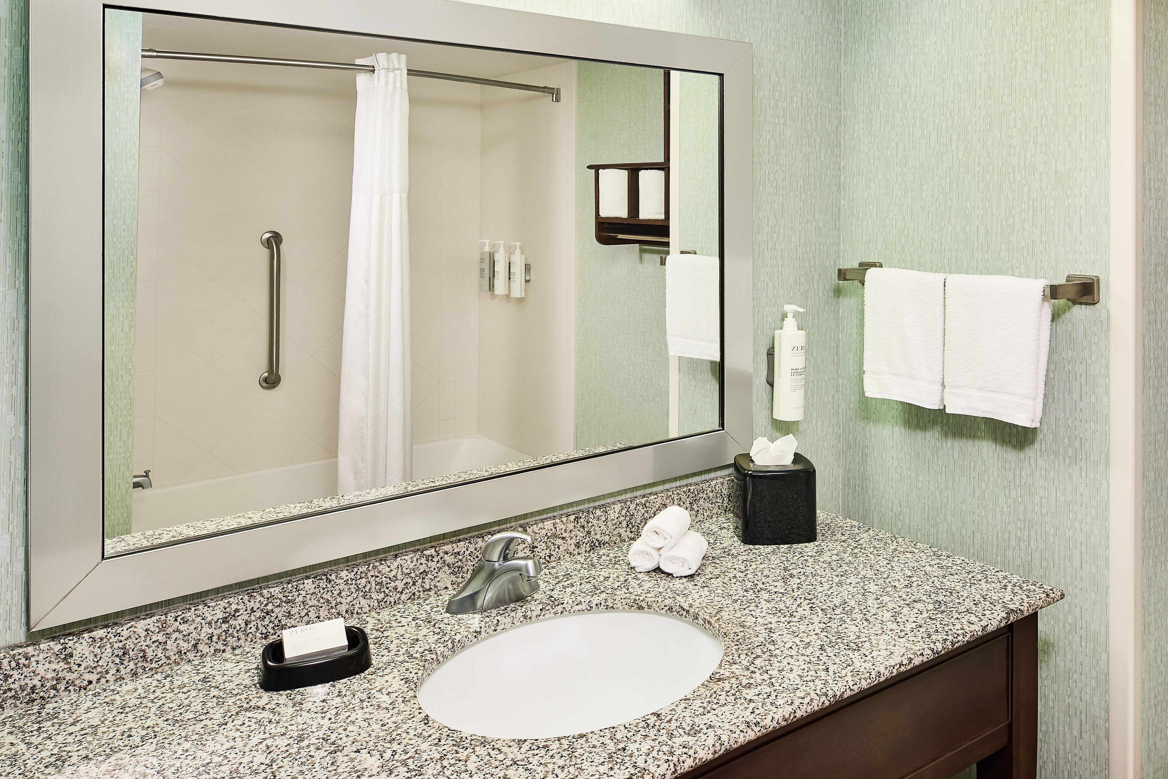 A bathroom with a large mirror, a sink, a towel rack, and a hand dryer.