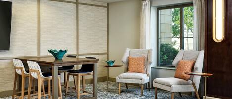 Una habitación moderna con una mesa de comedor, sillas, una pequeña mesita auxiliar, un ventanal con cortinas y una lámpara fijada a la pared.
