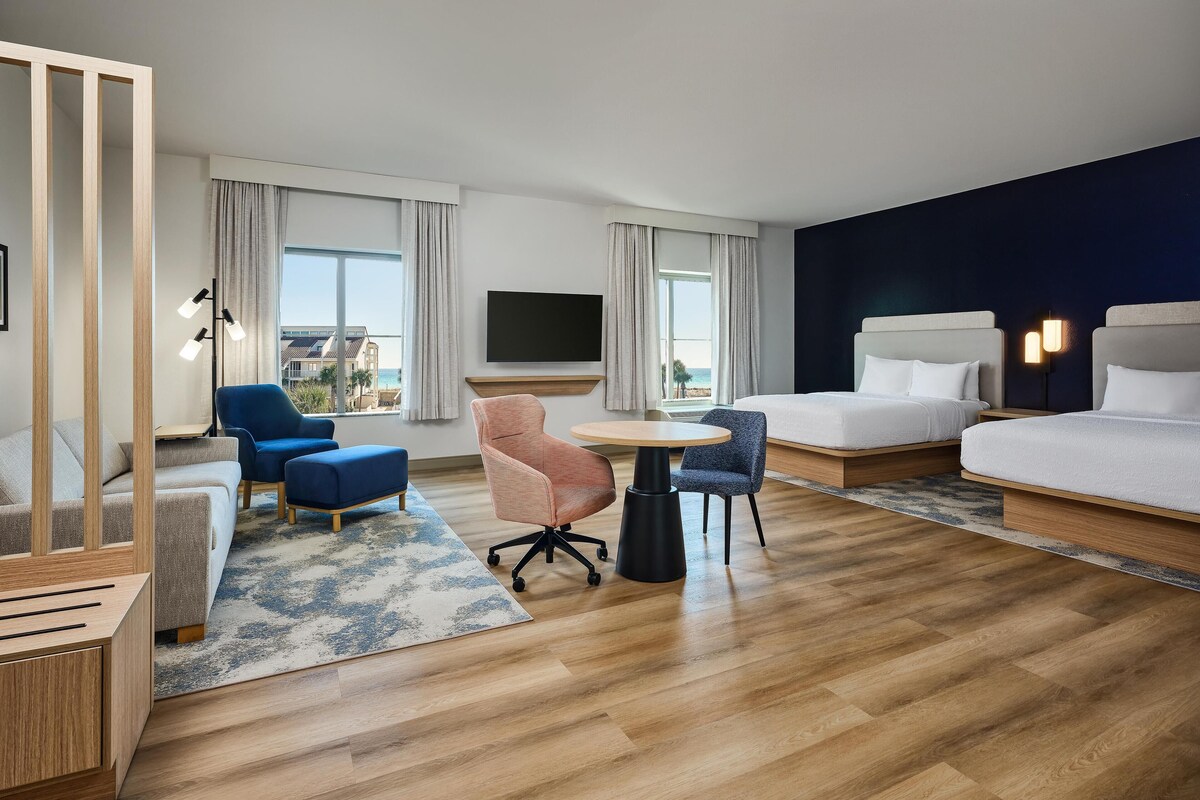 A modern hotel room with a sofa, two chairs, a round table, a bed, and a TV.