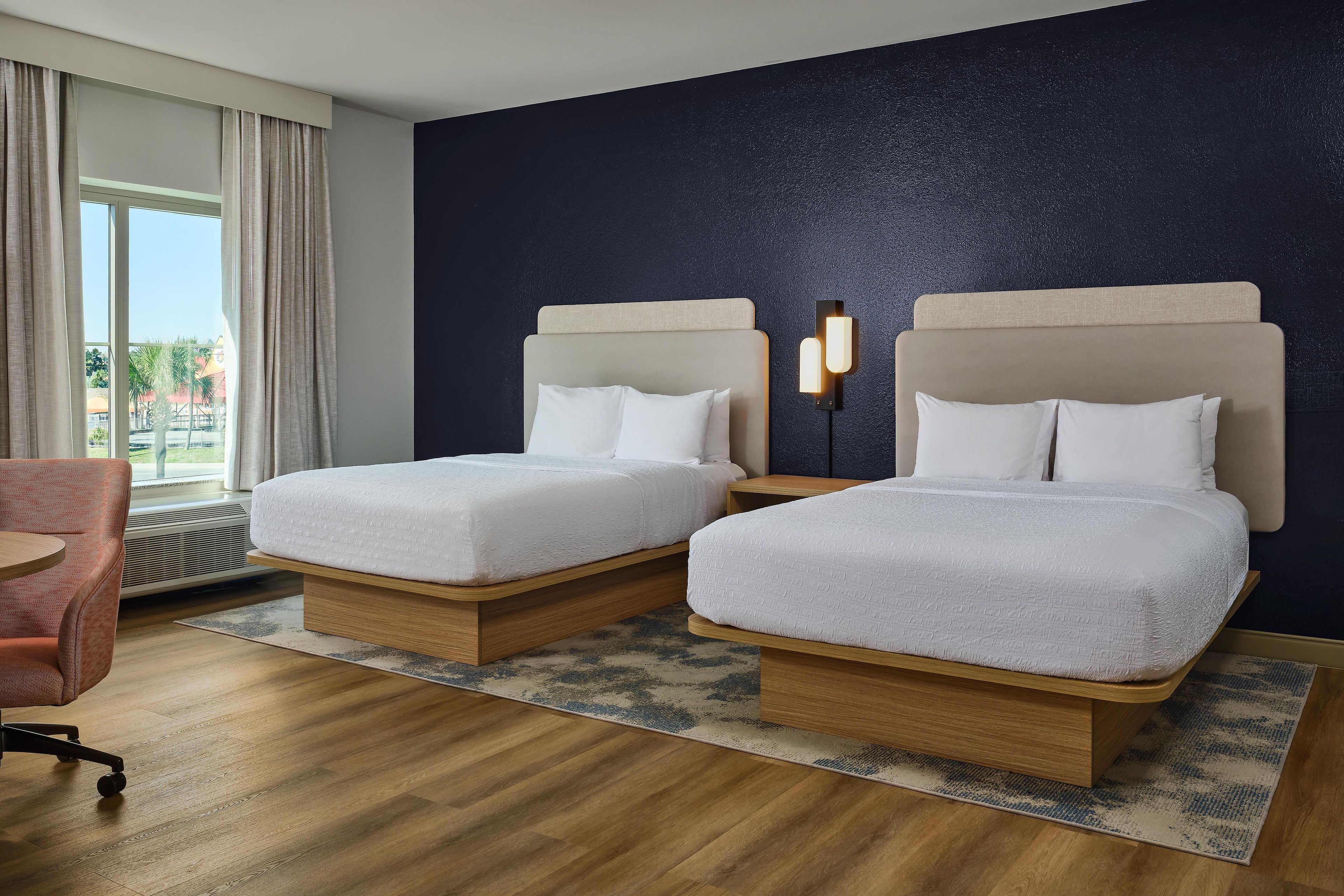 Une chambre d’hôtel avec deux lits, un bureau, une chaise et une vue sur l’extérieur.