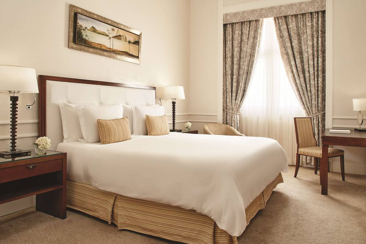 Une chambre d’hôtel avec un grand lit, deux tables de chevet avec des lampes, une chaise, un bureau et un tableau au mur.