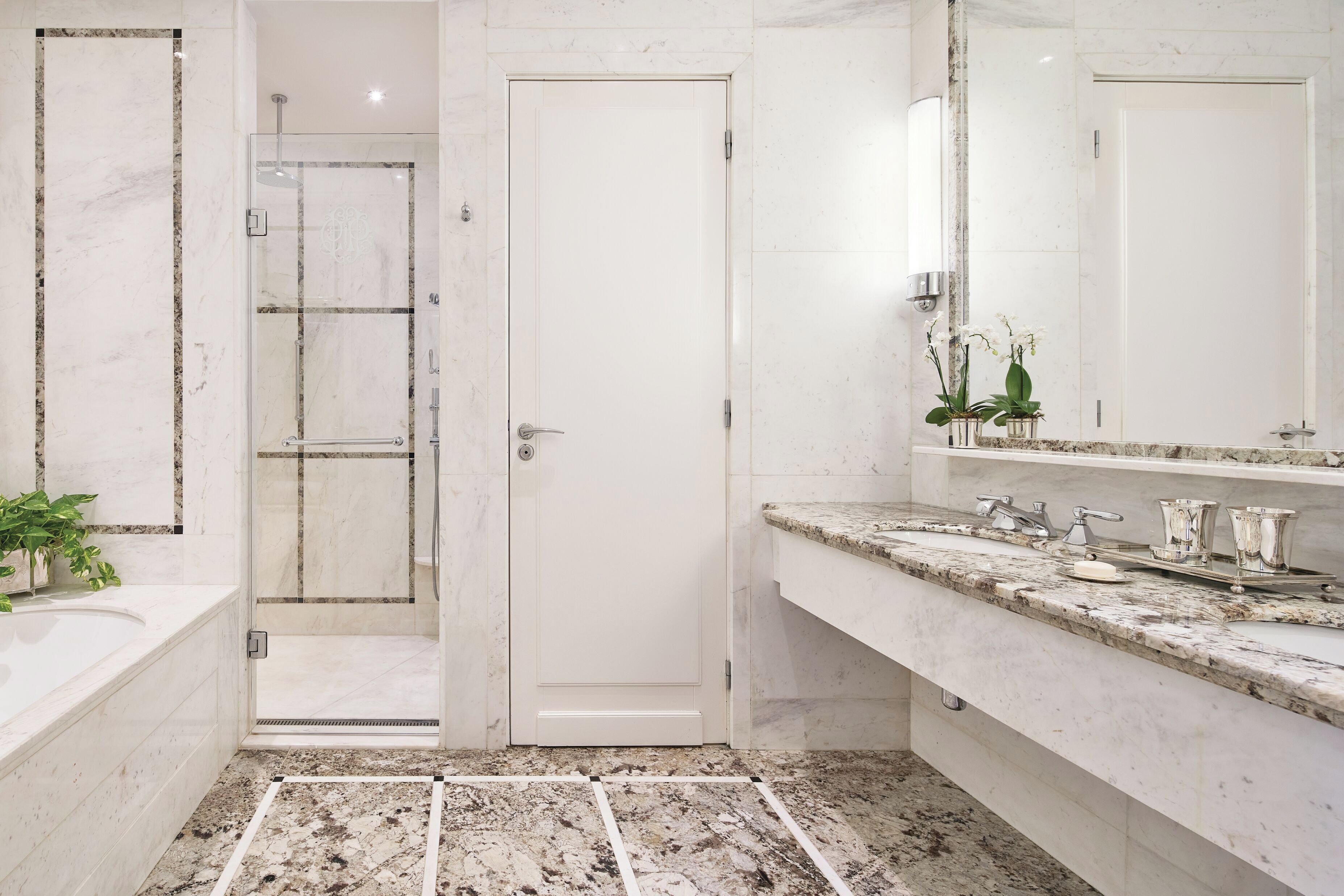 Un baño con ducha, lavabo, espejo y suelo de mármol.