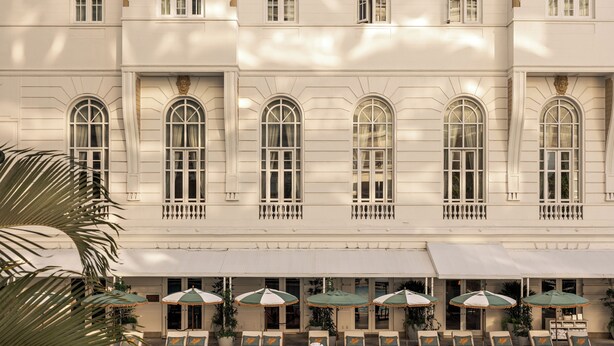 A large building with multiple arched windows and a swimming pool area with lounge chairs and umbrellas.