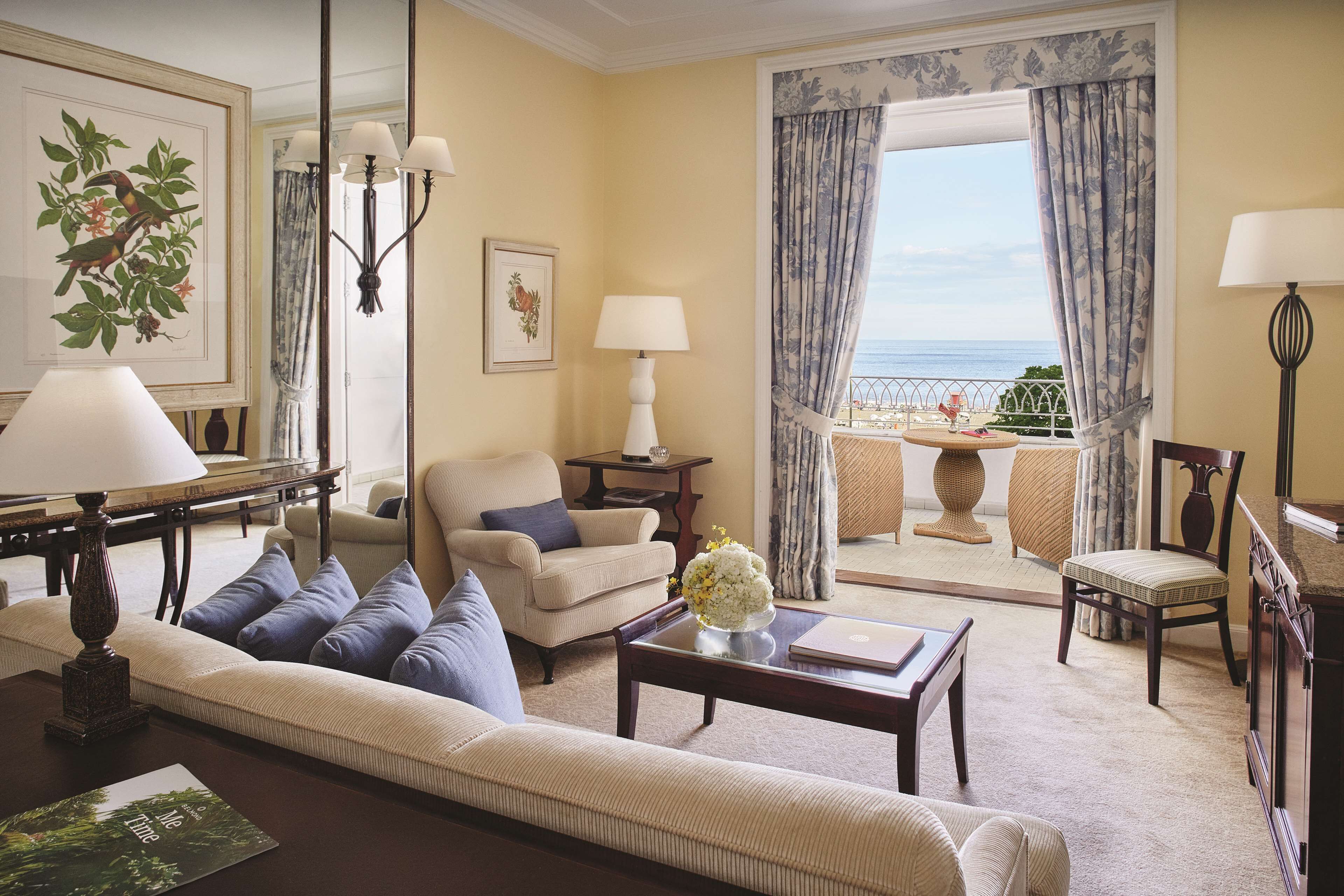 A living room with a sofa, armchairs, a coffee table, and a view of the sea through a large window.