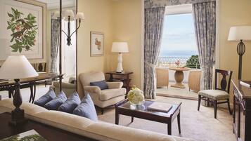 A living room with a sofa, armchairs, a coffee table, and a view of the sea through a large window.