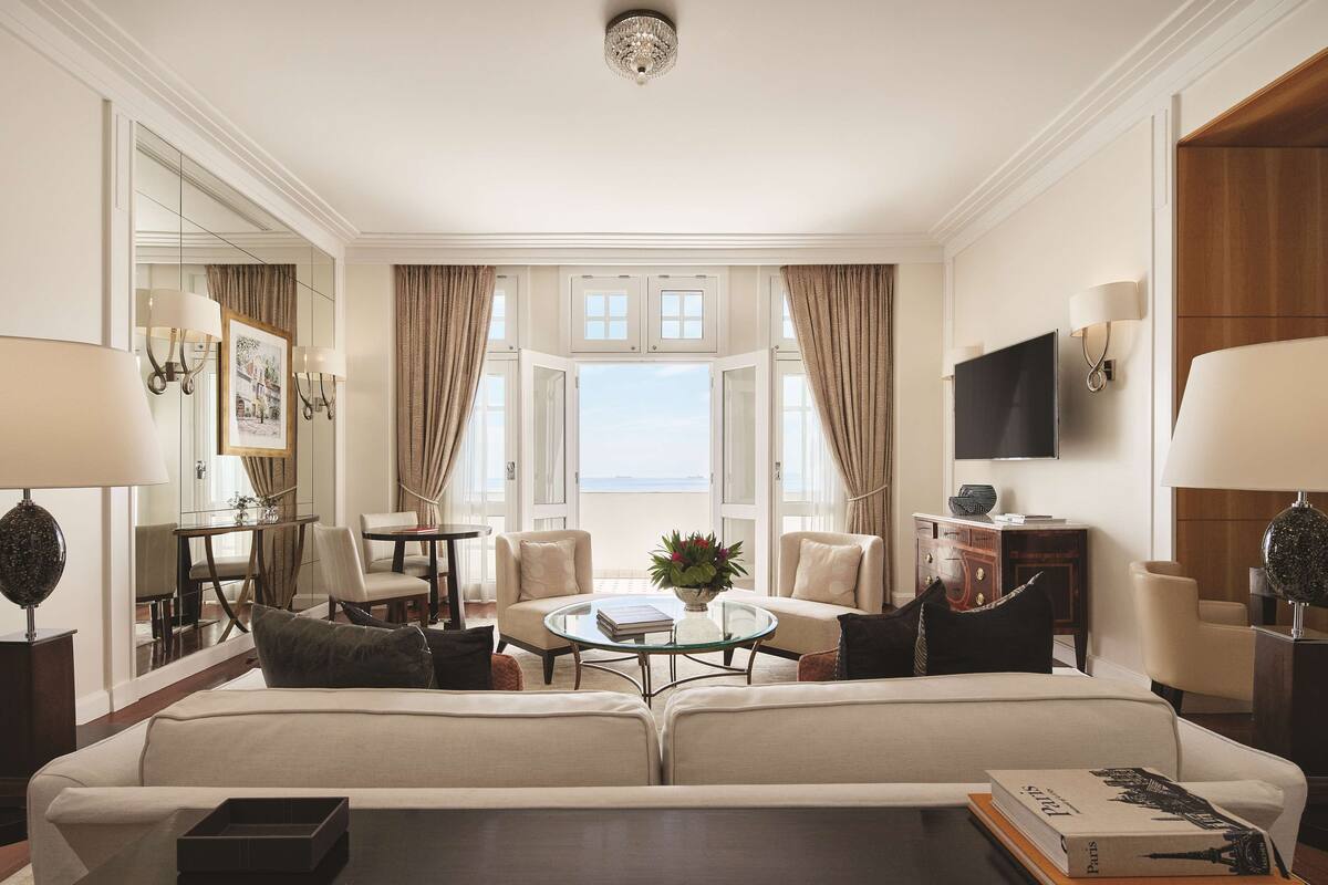 Une chambre d’hôtel spacieuse, dotée d’un grand lit, d’une table basse ronde, d’un coin repas et offrant une vue sur la mer.