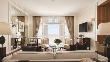 A hotel room with a sofa, a round coffee table, a TV, and a large window with curtains.