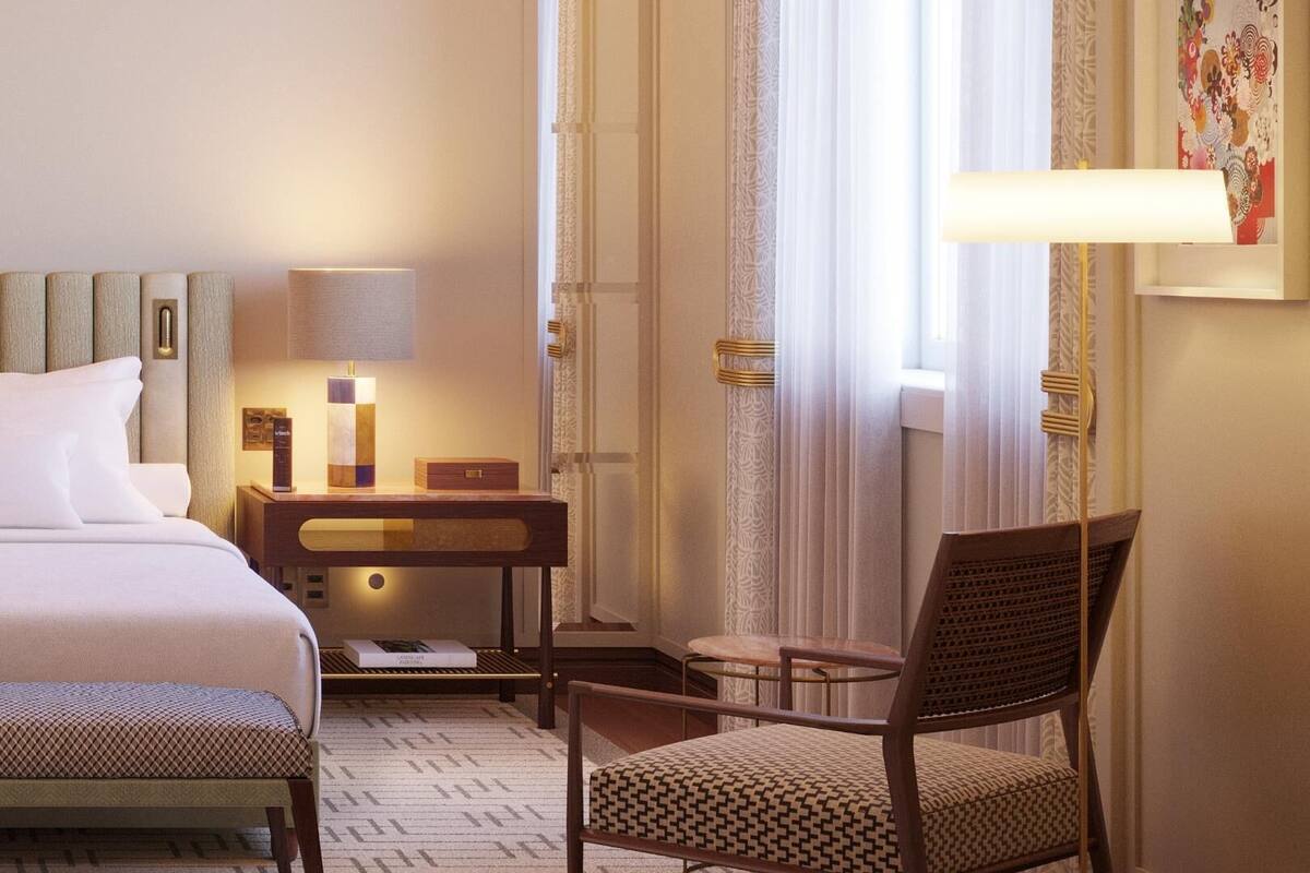 Une chambre d’hôtel avec un lit, un bureau, une chaise, une lampe et une fenêtre avec des rideaux.