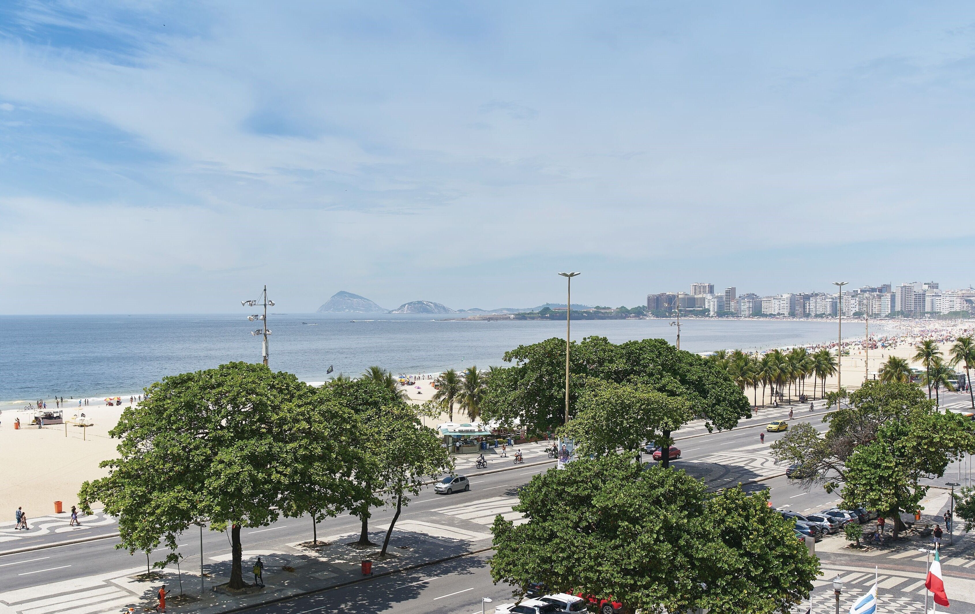 Paisagem costeira com praia, palmeiras e céu claro.