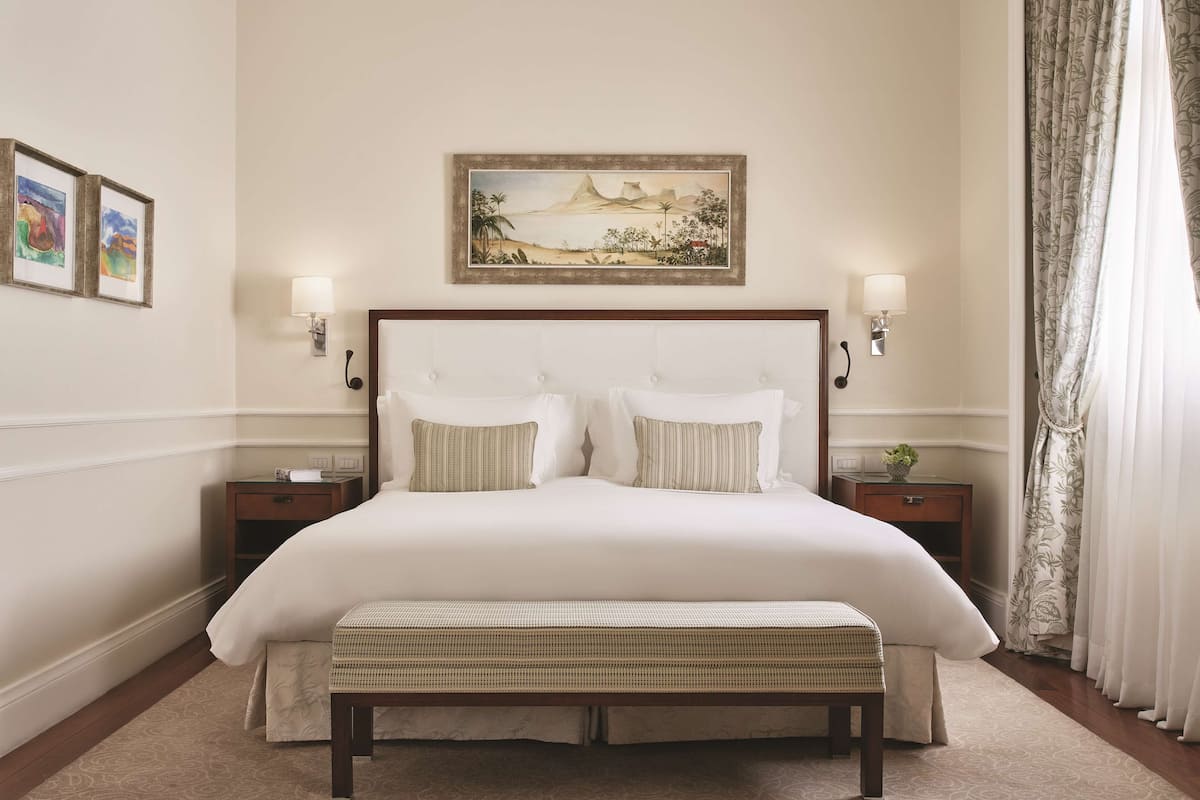 Une chambre à coucher bien rangée, avec un grand lit, deux tables de chevet, un banc et un tableau accroché au mur.