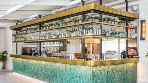 A bar area with a teal textured counter, multiple shelves of bottles, and potted plants.