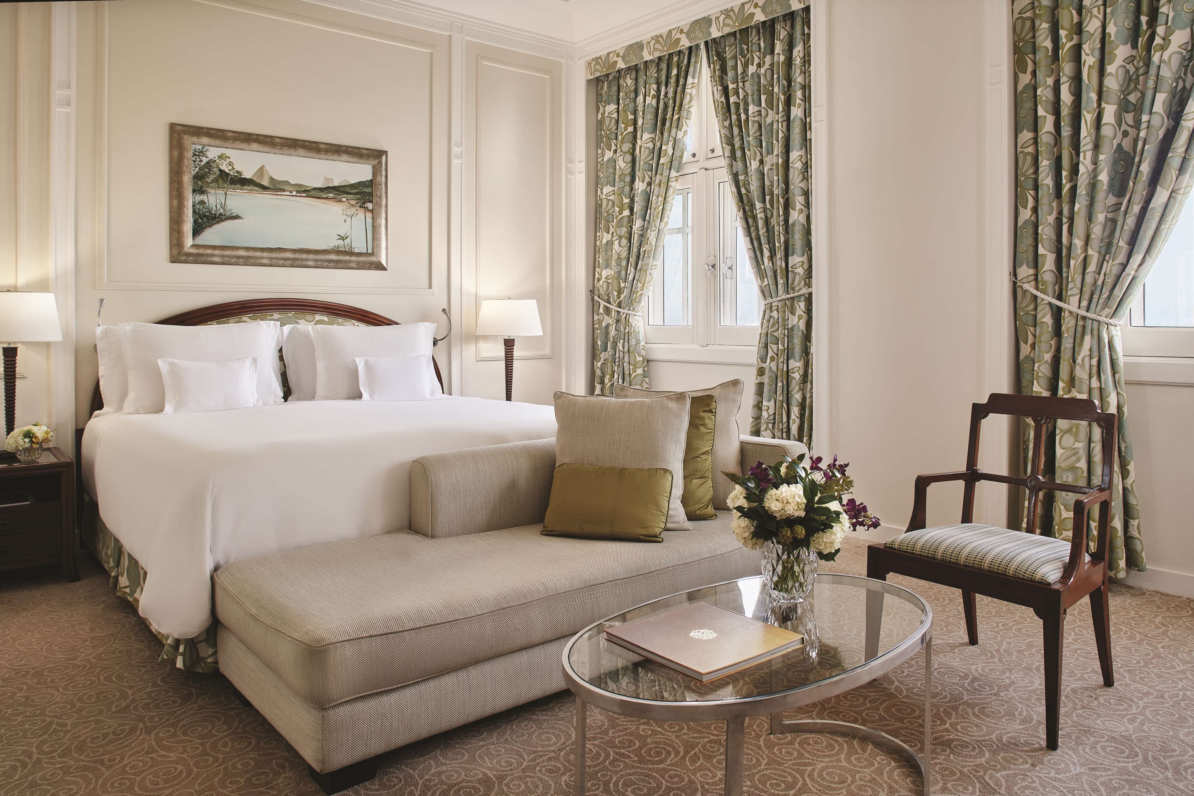 Een hotelkamer met een bed, een bank, een stoel, een glazen salontafel en een schilderij aan de muur.