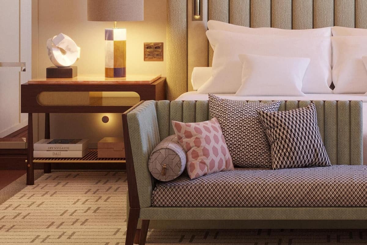 Une chambre d’hôtel comprenant un lit, une table de chevet avec une lampe, un canapé agrémenté de coussins à motifs et un élément décoratif mural.