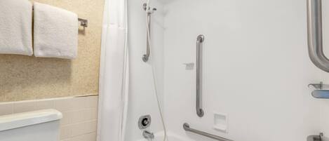 A bathroom with a white bathtub, a shower with a handheld showerhead, and grab bars.
