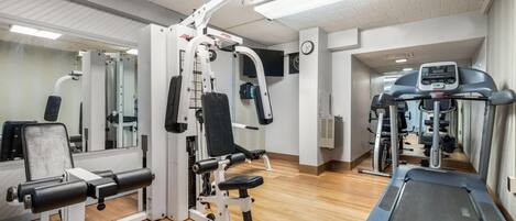 Une salle de sport équipée de matériel d’exercice, d’un tapis de course et d’un miroir.