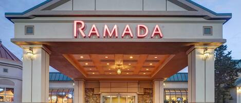 A hotel entrance with a prominent "RAMADA" sign, a covered entrance area, and a stone facade.