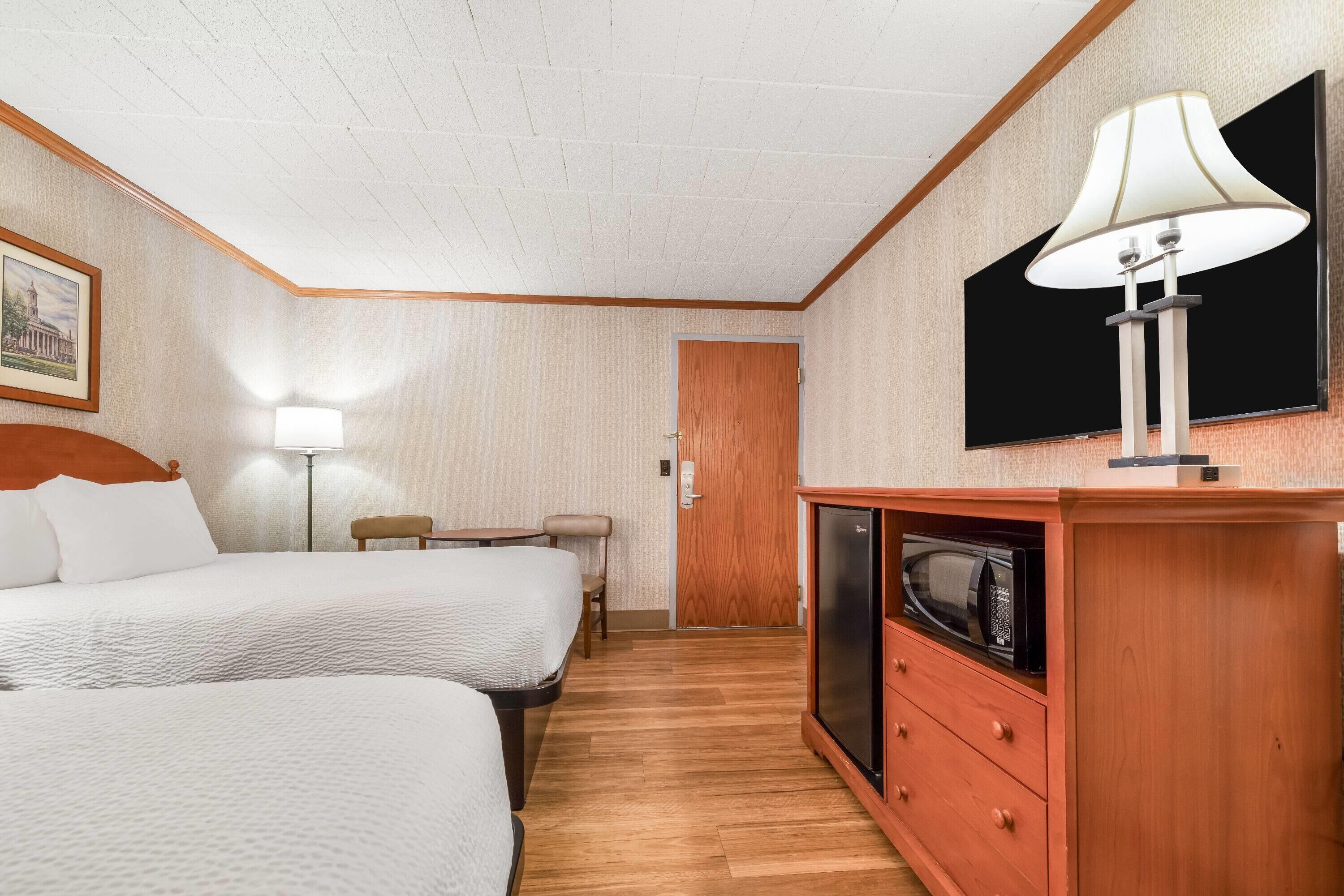 A hotel room with two beds, a desk, a chair, a TV, and a microwave.