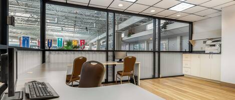 A modern office space with a large window, a desk with a keyboard, two chairs, and a kitchenette area.