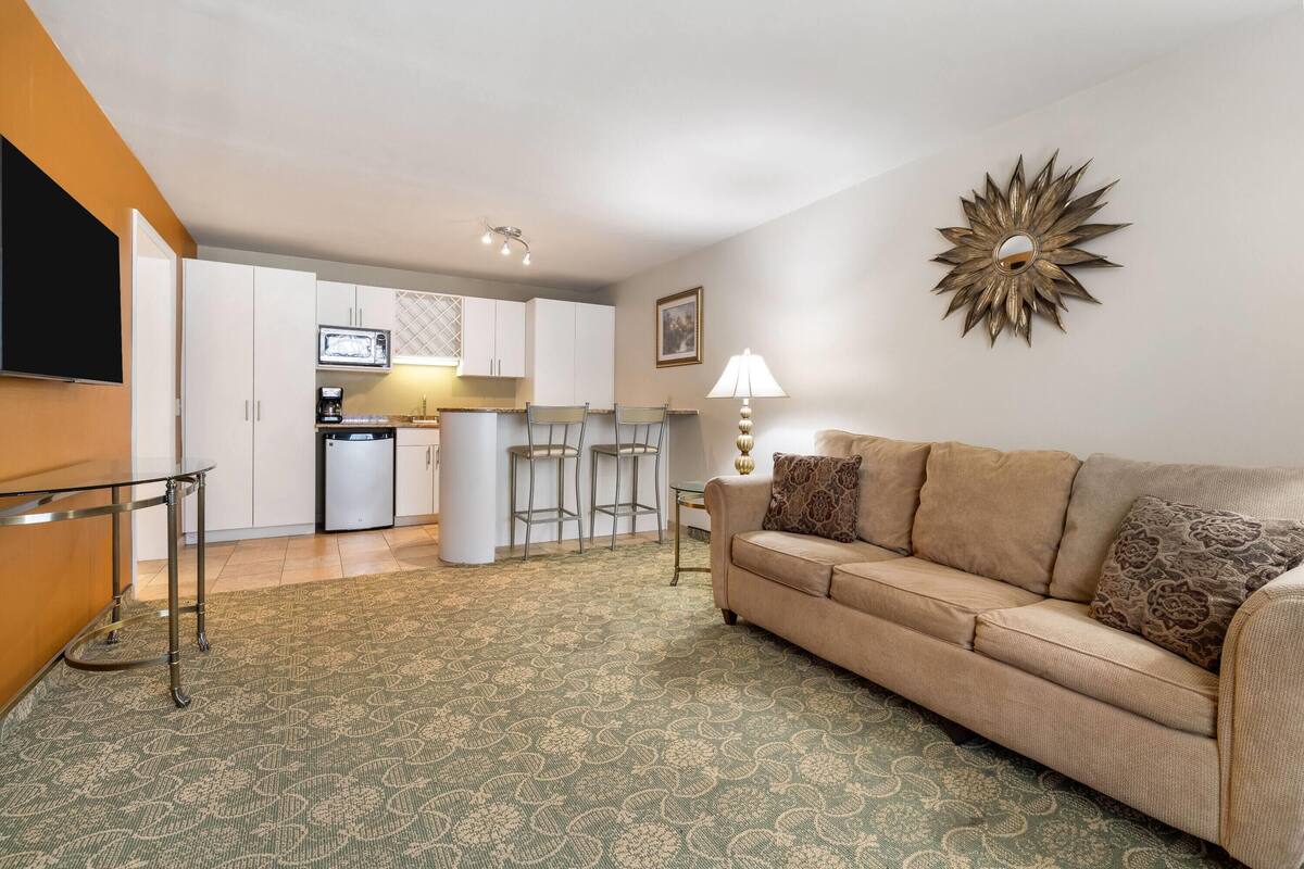 A living room with a sofa, a coffee table, a TV, and a kitchen area in the background.