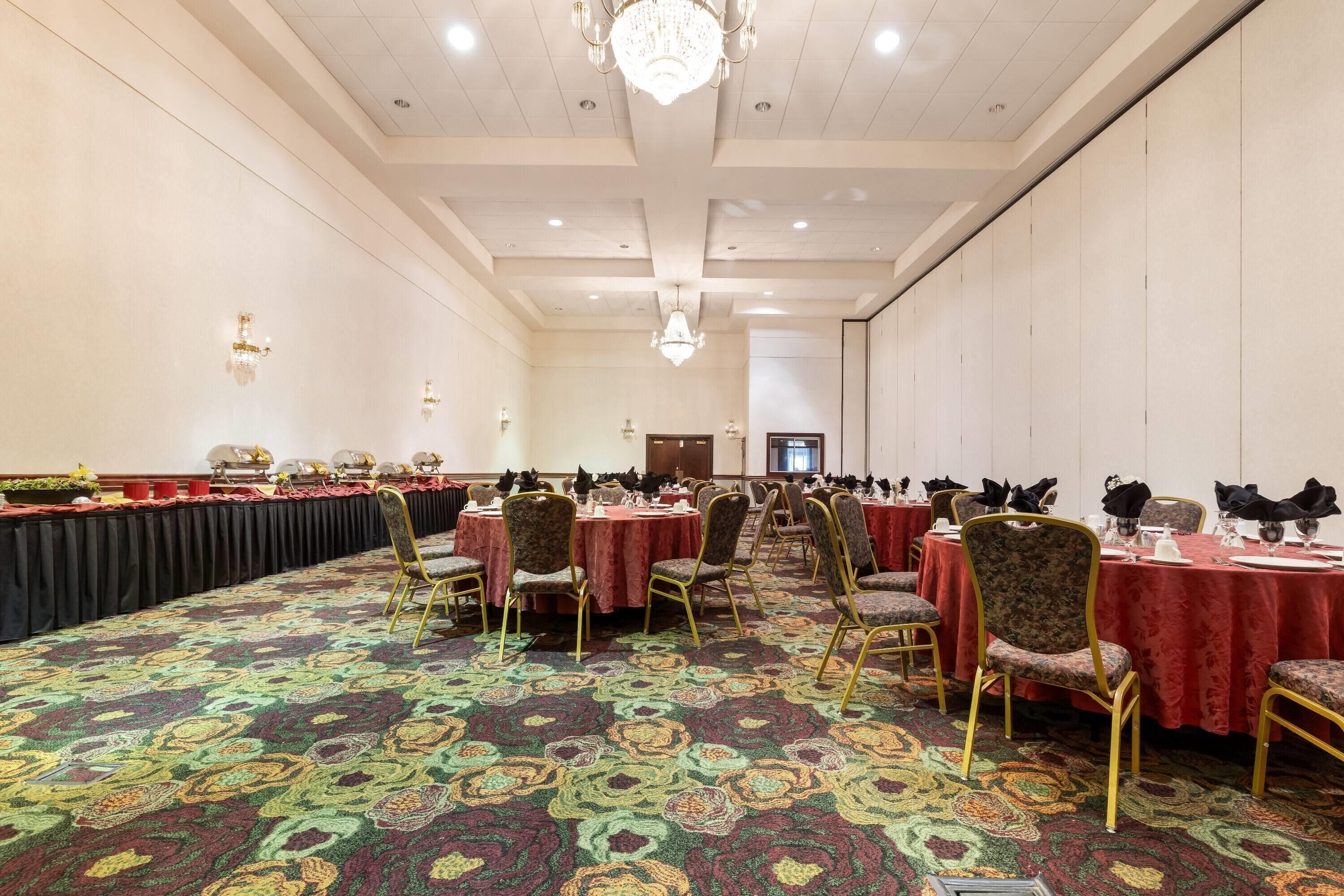 A banquet hall with round tables, chairs, and a patterned carpet.