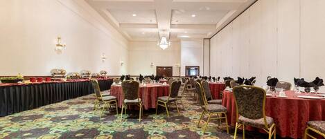 A banquet hall with round tables, chairs, and a patterned carpet.