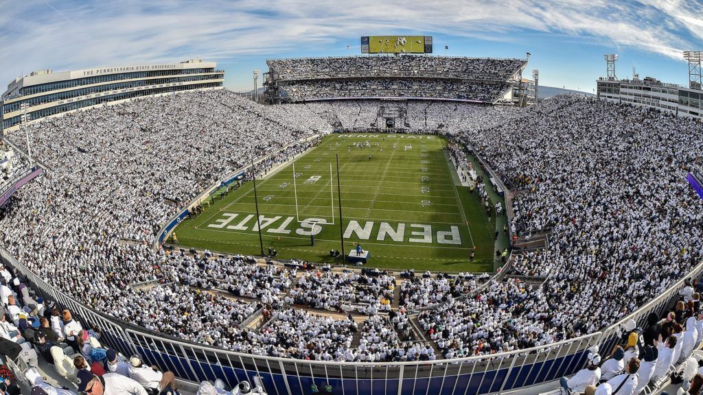 A large stadium with multiple tiers of seating, a football field, and a scoreboard.