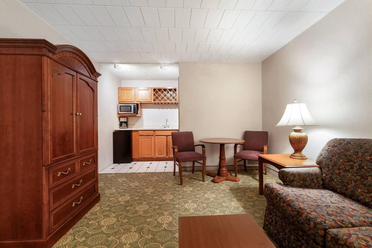 A compact living space with a wooden cabinet, a patterned sofa, a small round table, and a lamp.