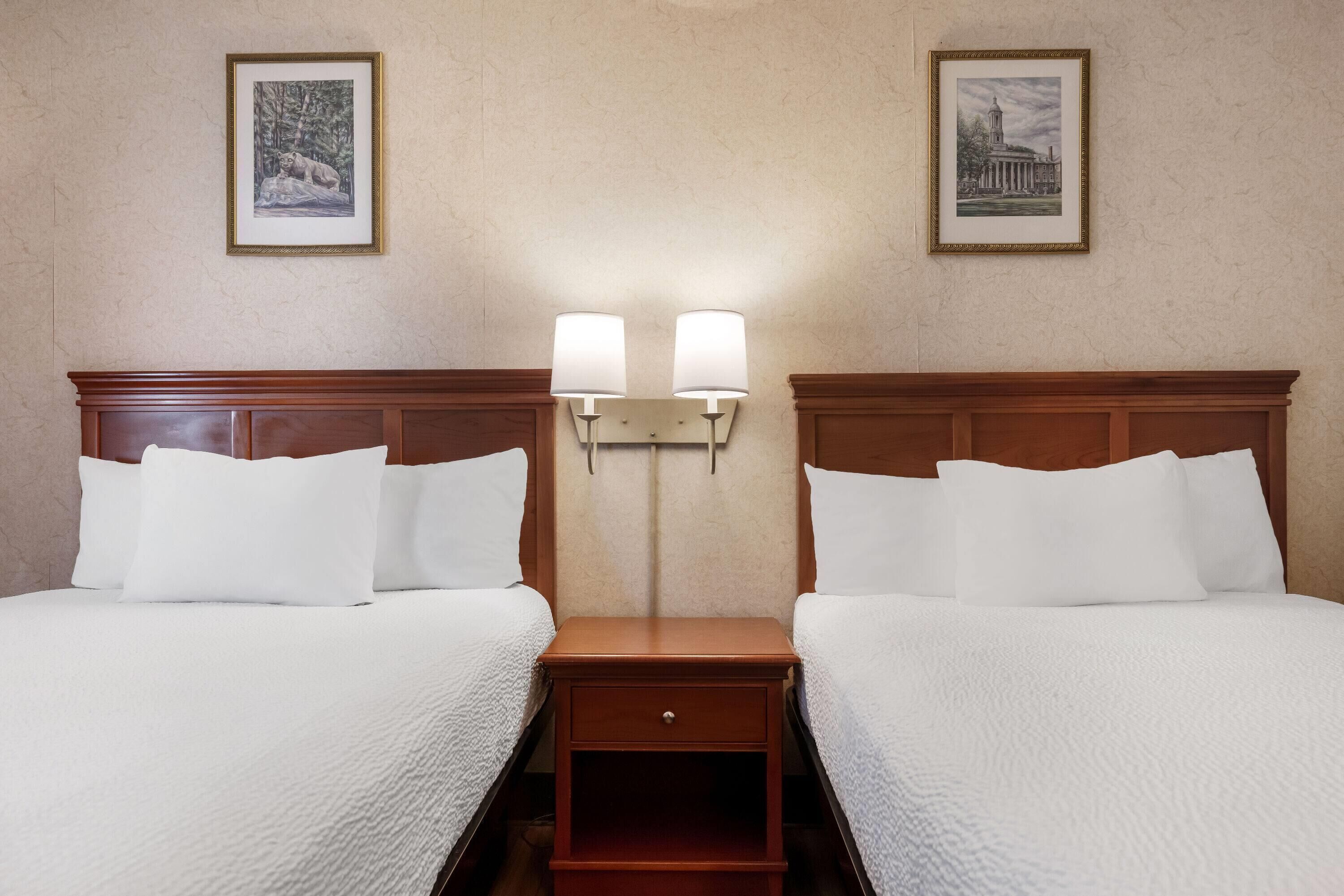 A hotel room with two beds, a nightstand with a lamp, and framed pictures on the wall.