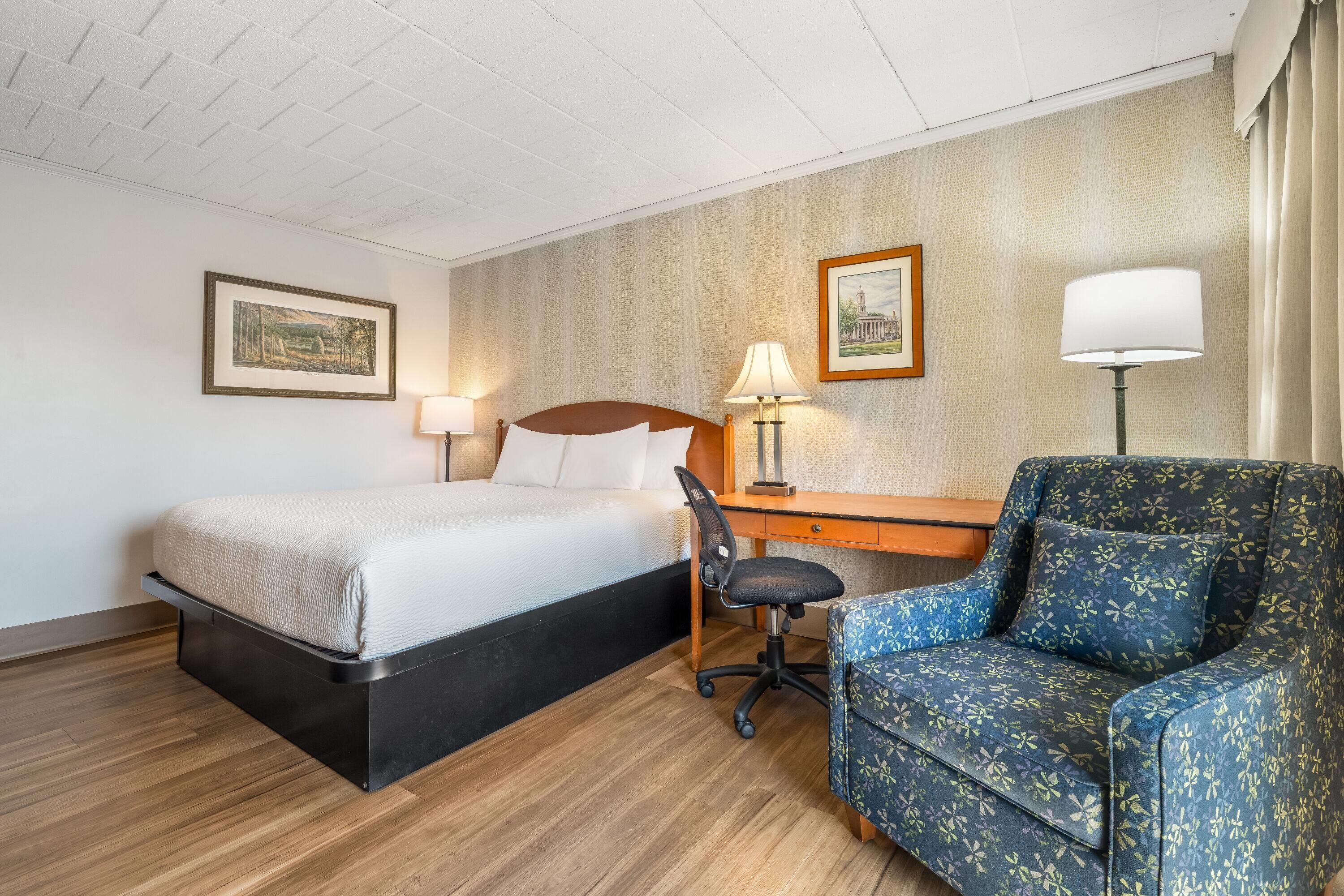 Una habitación de hotel con una cama, un escritorio, una silla y dos lámparas.