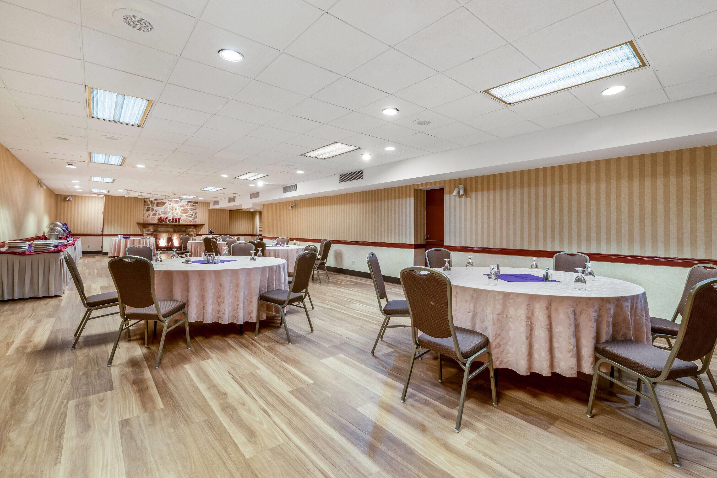 A conference room with round tables and chairs, a stone fireplace, and a wooden panel wall.