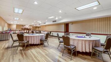 A conference room with round tables and chairs, a stone fireplace, and a wooden panel wall.