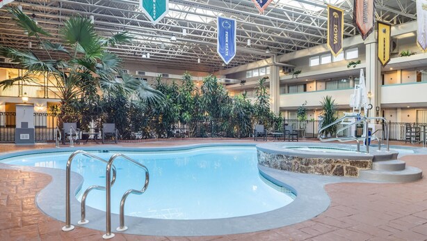 Une piscine intérieure dotée de plusieurs niveaux de balcons, entourée de plantes d’intérieur et agrémentée d’espaces de détente.