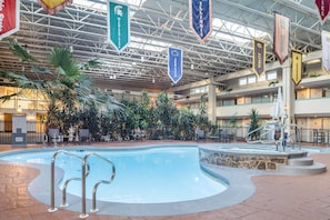 An indoor swimming pool with multiple levels of balconies, surrounded by indoor plants and seating areas. - Ramada by Wyndham State College Hotel & Conference Center (State College)