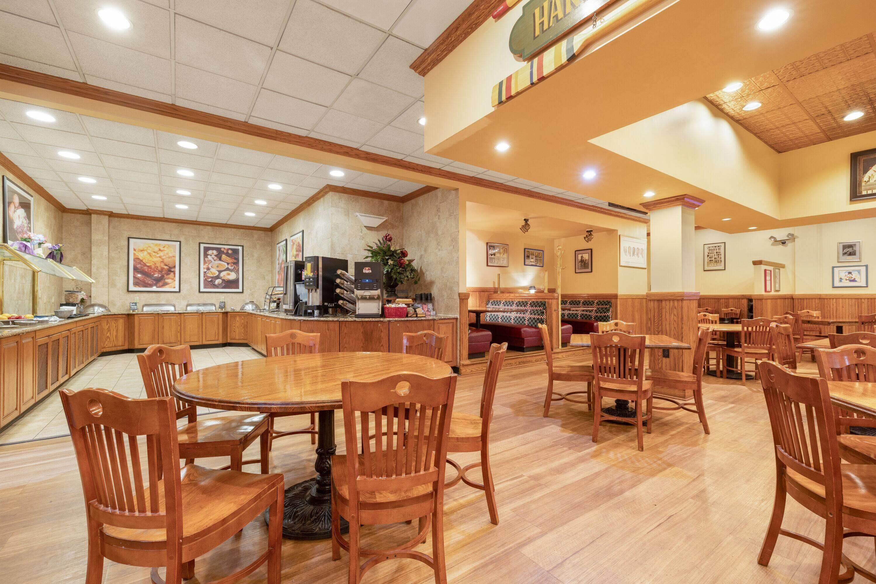 Un comedor amplio con mesas y sillas de madera, una zona de cocina con estilo buffet, y un rincón de descanso con bancos acolchados.