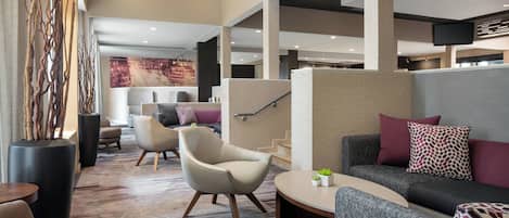 A modern hotel lobby with seating areas, a staircase, and a large wall mural.