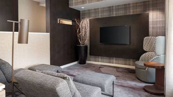 A modern living room with grey upholstered sofas, a flat-screen TV mounted on the wall, and a tall floor lamp.