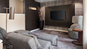 Una sala de estar moderna con sofás tapizados en gris, un televisor de pantalla plana montado en la pared y un jarrón decorativo con ramas.