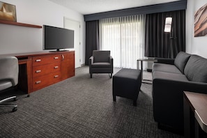 A hotel room with a flat-screen TV, a sofa, a chair, a desk with drawers, and a large window with curtains. - Courtyard Fremont Silicon Valley (Fremont)