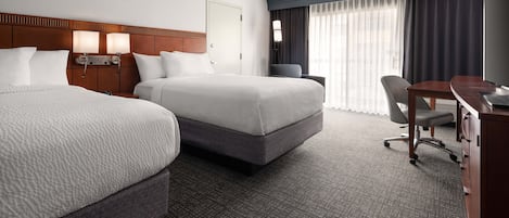A hotel room with two beds, a desk, a chair, and a large window with curtains.