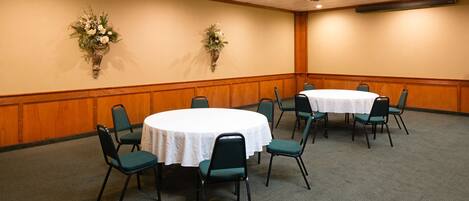 A conference room with a round table, green chairs, and two wall-mounted flower arrangements.