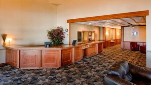 A reception area with a wooden reception desk, a potted plant, and a patterned carpet. - Red Lion Hotel & Conference Center Ellensburg (Ellensburg)