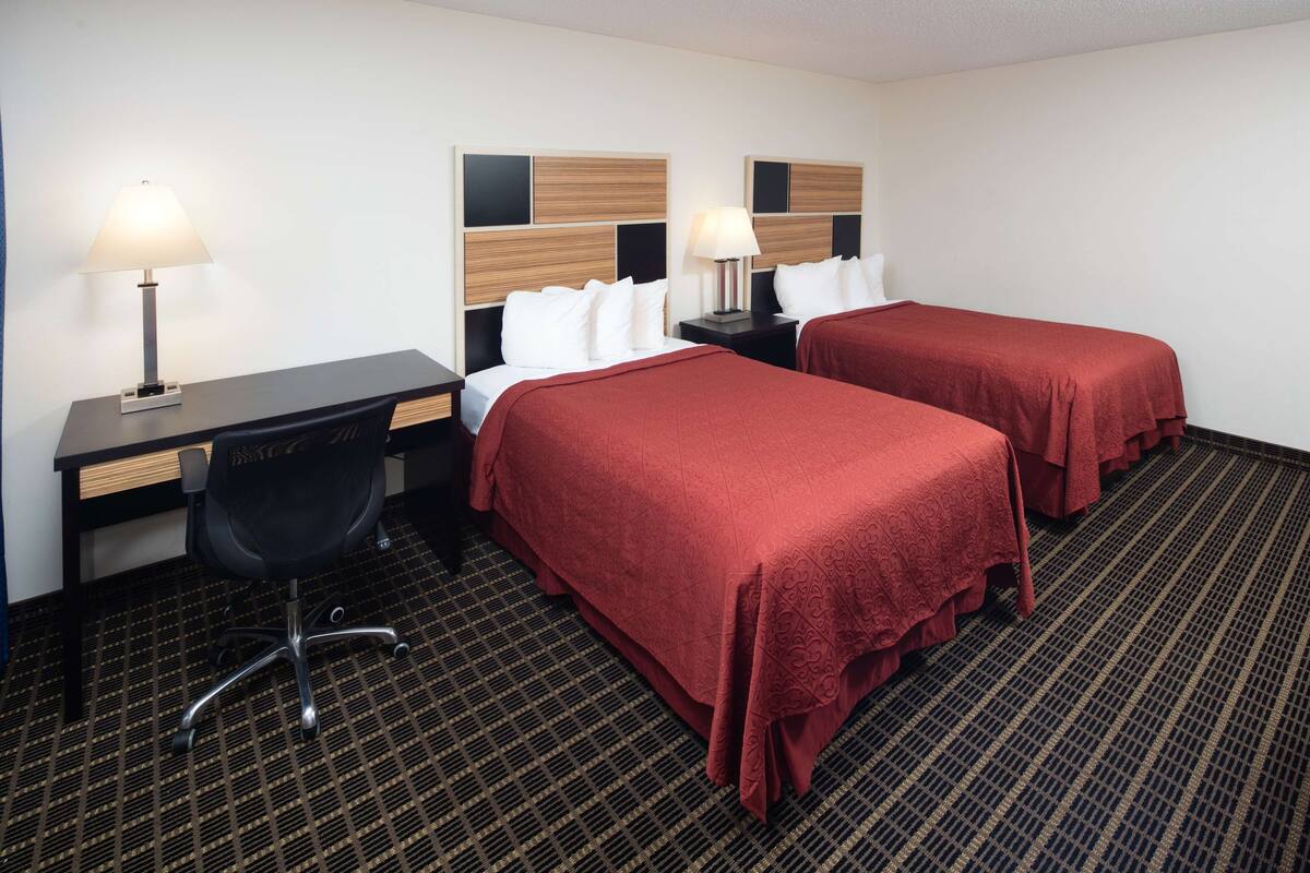 Ein Hotelzimmer mit zwei Betten, einem Schreibtisch, einem Stuhl und zwei Nachttischen mit Lampen.