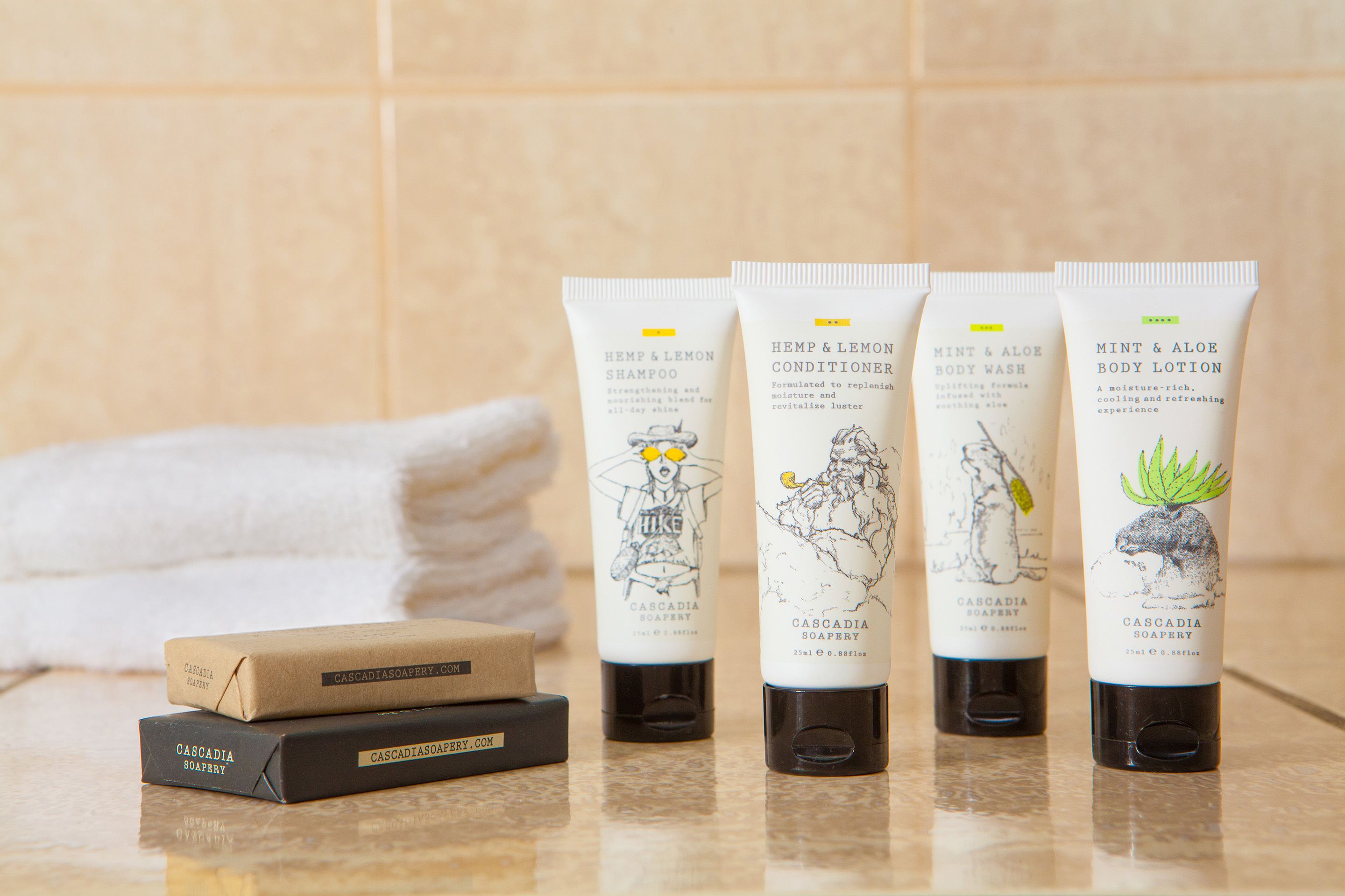 Cuatro tubos de productos de Cascadia Soapery y dos pastillas de jabón sobre una encimera de baño.