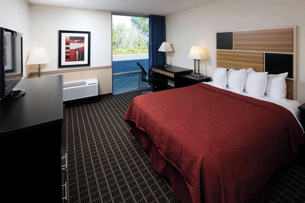 Ein Hotelzimmer mit einem großen Bett, einem Schreibtisch, einem Sessel, einem Fernseher und einem Fenster mit Aussicht ins Freie.