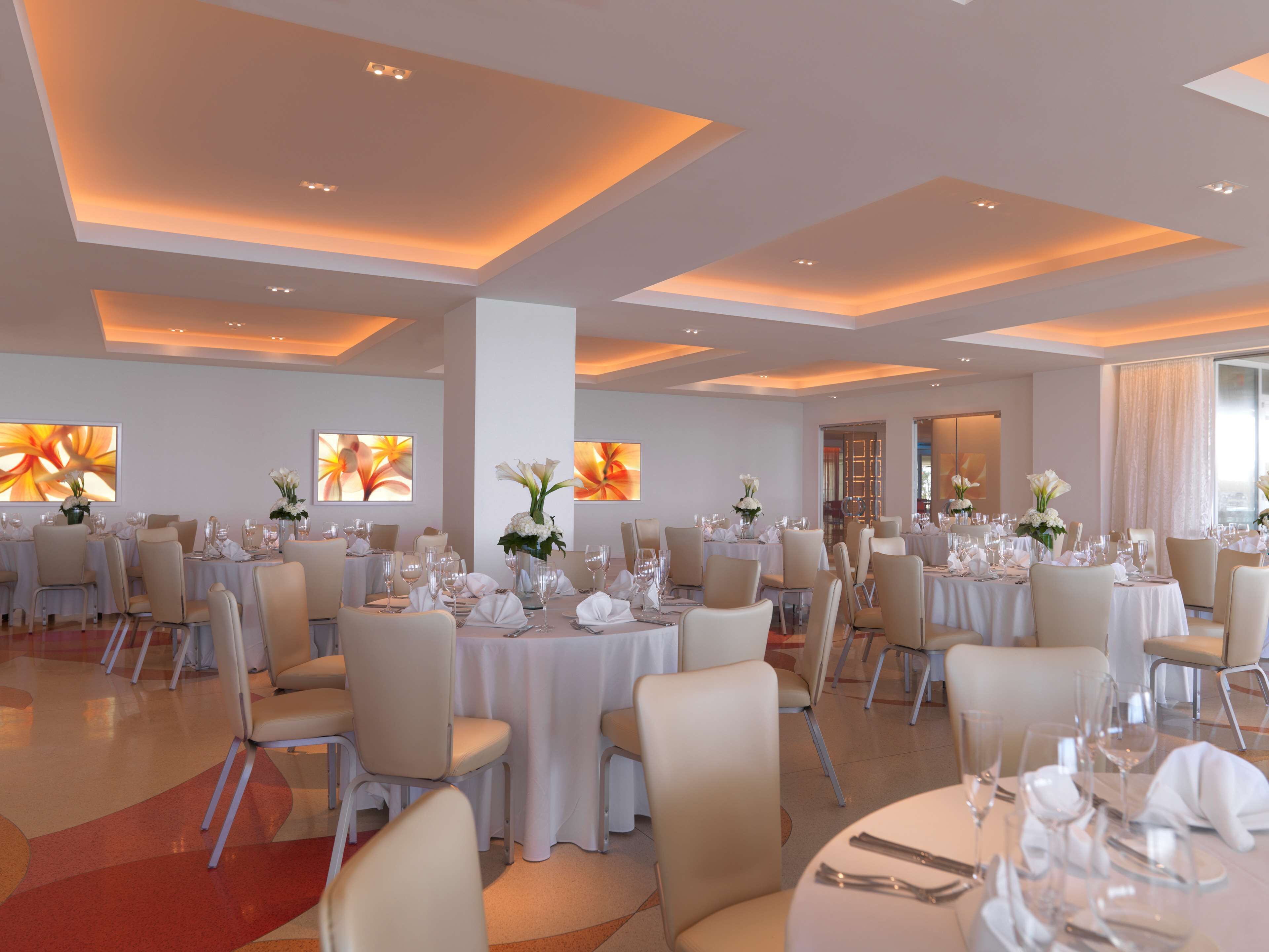 Un vaste espace dédié à la salle à manger, avec plusieurs tables rondes dressées pour un événement formel, nappes blanches et décorations de table élégantes.