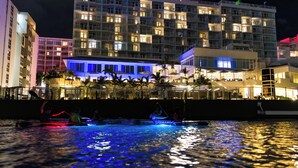 Hotel frente al agua con varios balcones y un área de piscina con agua iluminada.