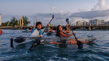 Due persone su un kayak in mezzo all'acqua, con un ponte e degli edifici sullo sfondo.