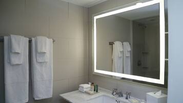A modern bathroom with a large mirror, white towels, a sink, and toiletries.