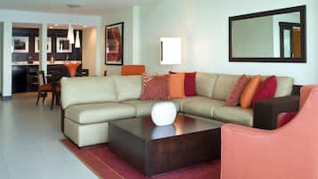 A modern living room with a sectional sofa, a coffee table, and a dining area in the background.