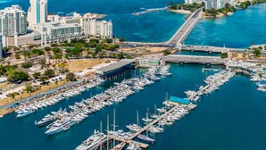 Vista aérea de un puerto deportivo con numerosas embarcaciones amarradas, rodeado de edificios altos y un paisaje urbano costero.